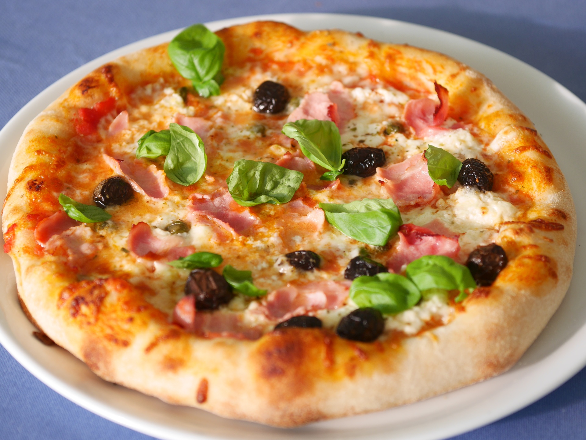 Pizza mit Burrata, Prosciutto, Oliven, Kapern,
              Basilikum